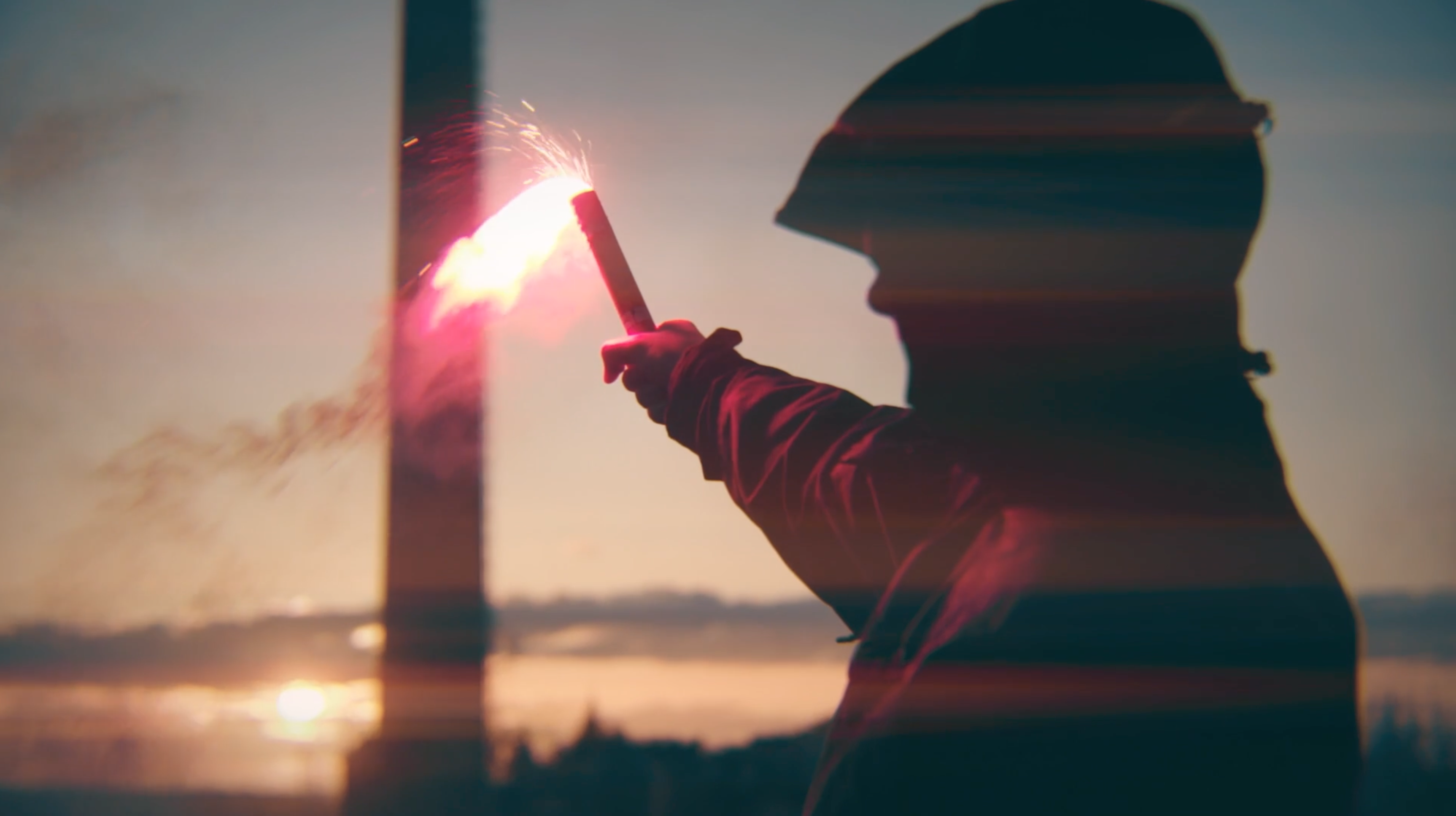 Silhouetted figure holding a red flare at sunset